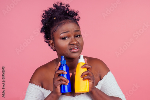 african american woman applying cream shoosing between two products in studio pink background photo