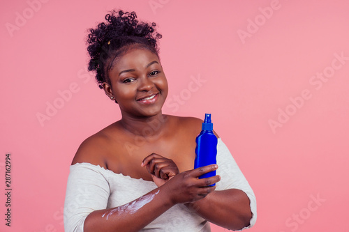 african american woman applying cream shoosing between two products in studio pink background