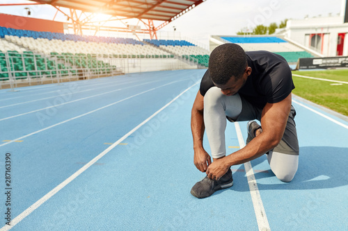 Sportsman ties his trainers, sitting on the running track, preparing. Concept of marathon and competition. copy space. rest.full length photo