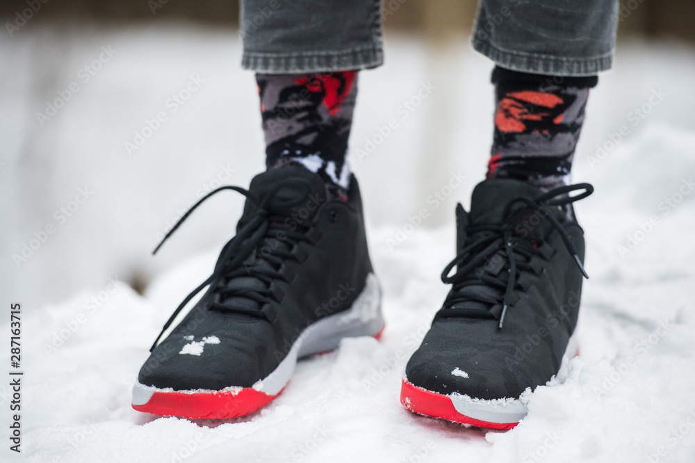 Male legs in athletic shoes, cropped jeans and fashionable socks standing on snow. Stylish and trendy winter look. Male legs in athletic shoes, cropped jeans and fashionable socks standing on snow. Stylish and trendy winter look.