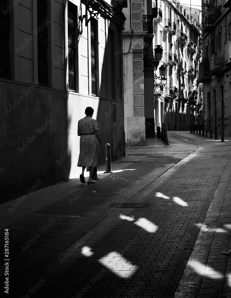 Woman with long dress walking on the street between lights and shadows Woman with long dress walking on the street between lights and shadows