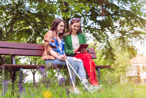 Two friends in a park, one with a broken feet and crutches