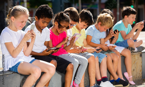 Positive kids sitting at urban street with mobile devices