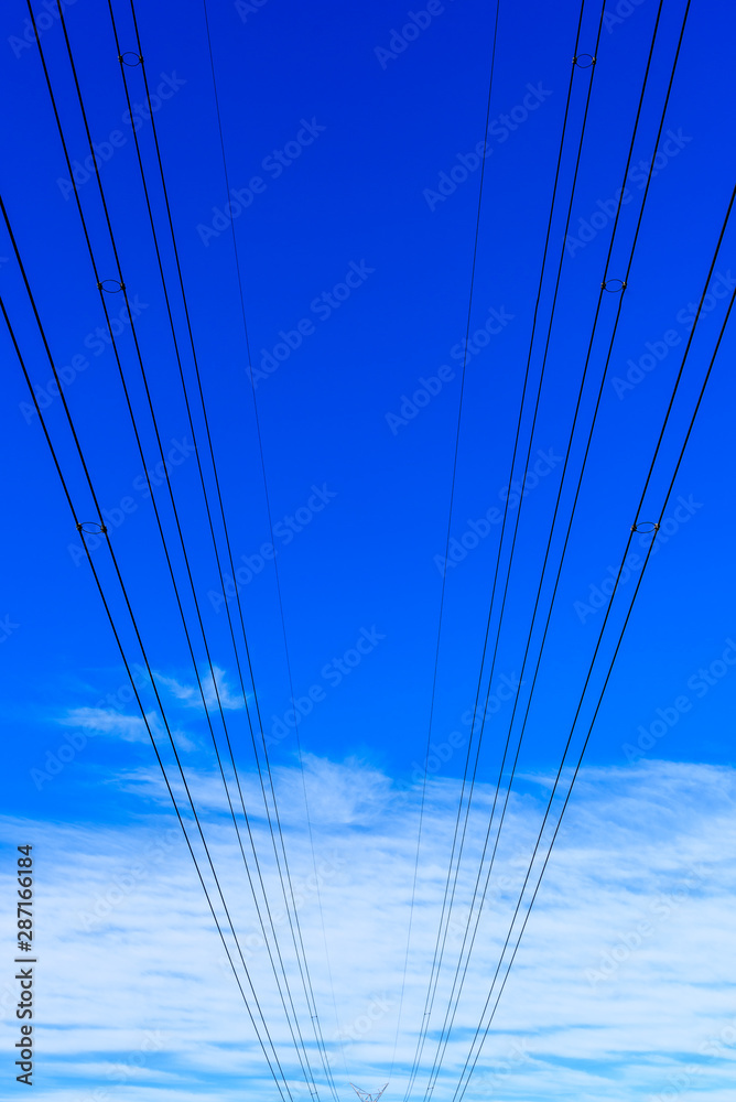 Electricity powerlines against a blue sky with light white clouds