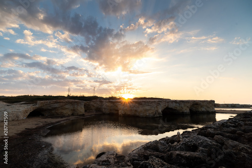 Shot of the sun rising behind the rocks at Cirica Bay at sunrise. Cirica is a beautiful nature seaside place made of cliffs, rocks and sand in the southern Sicily, Italy