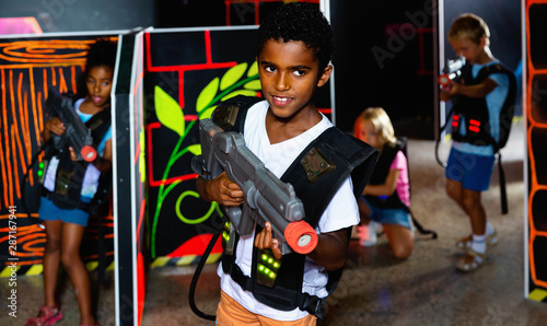 Portrait of tweenager boy with laser gun having fun on dark lasertag arena