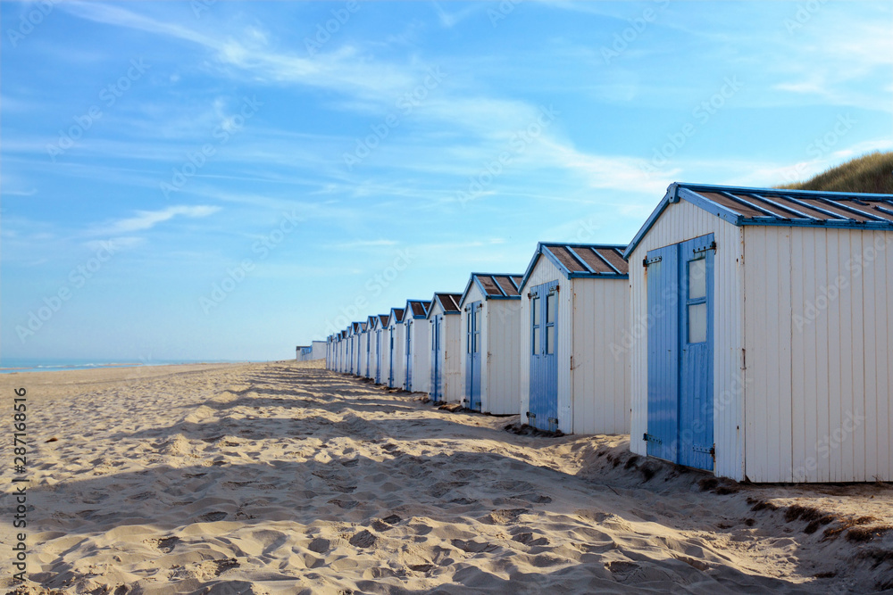 Row of white and blue beach huts on the beach of island Texel in the Netherlands with blue sky on sunny day Row of white and blue beach huts on the beach of island Texel in the Netherlands with blue sky on sunny day