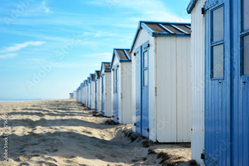 Row of white and blue beach huts on the beach of island Texel in the Netherlands with blue sky on sunny summer day, selective focus with focus on right hut and copy space to the left © Firn