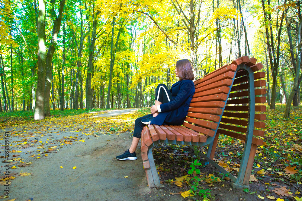 girl sits on a bench in the autumn park girl sits on a bench in the autumn park
