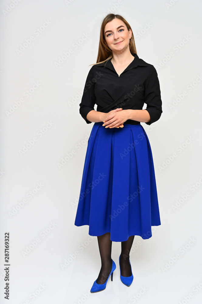 Full length vertical portrait of a cute brunette middle-aged manager woman with beautiful curly hair in a business suit and blue skirt on a white background. Beauty, brightness, smile. Full length vertical portrait of a cute brunette middle-aged manager woman with beautiful curly hair in a business suit and blue skirt on a white background. Beauty, brightness, smile.