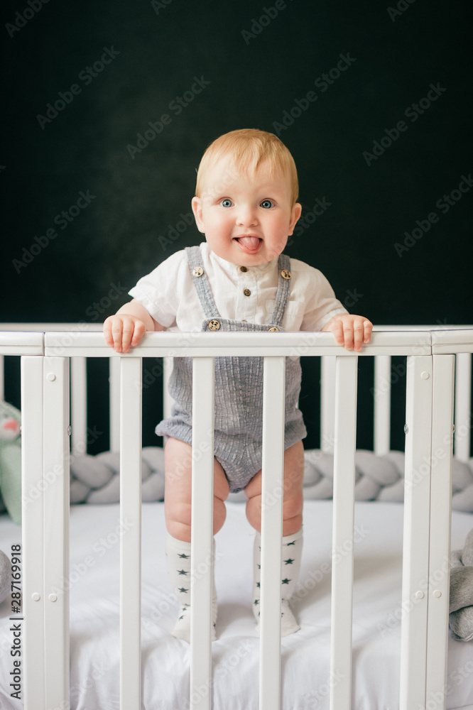 Portrait of funny baby standing in crib. Stylish baby boy standing alone in  cot over black background. Stock Photo | Adobe Stock