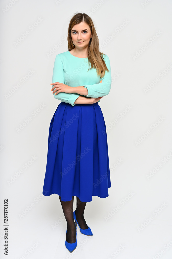 Full-length vertical portrait of a cute brunette middle-aged manager woman with beautiful curly hair in a business suit and blue skirt on a white background. Beauty, brightness, smile. Full-length vertical portrait of a cute brunette middle-aged manager woman with beautiful curly hair in a business suit and blue skirt on a white background. Beauty, brightness, smile.