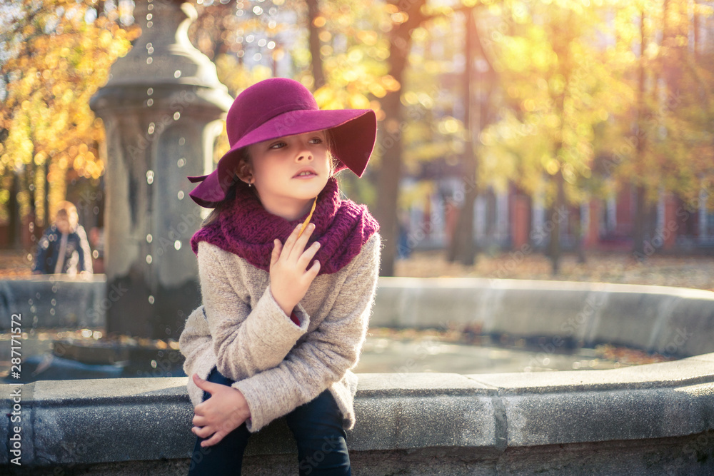 Girl in classic coat and hat in autumn park near the fountain. Autumn season, fashion, childhood.