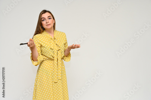 Portrait of a cute middle-aged manager brunette woman with beautiful curly hair in a yellow dress on a white background with a pen in her hands. Beauty, brightness, smile. photo