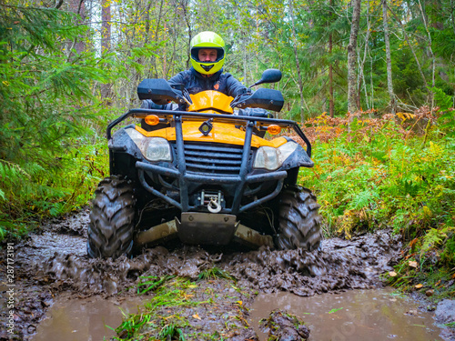 ATV racing. A man on a yellow quadrocycle. ATV tires in the mud. Man in a yellow helmet on a quad bike. A human came to the forest on an quadrocycle. ATV with a driver close-up. Extreme quad bike ride © Grispb