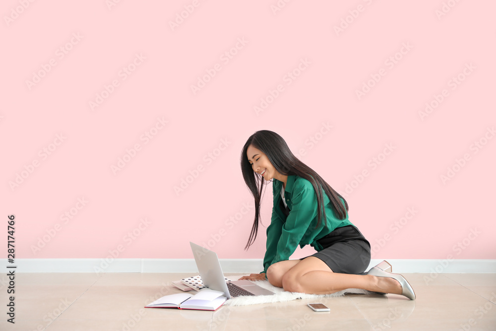 Young Asian blogger with laptop sitting near color wall Young Asian blogger with laptop sitting near color wall