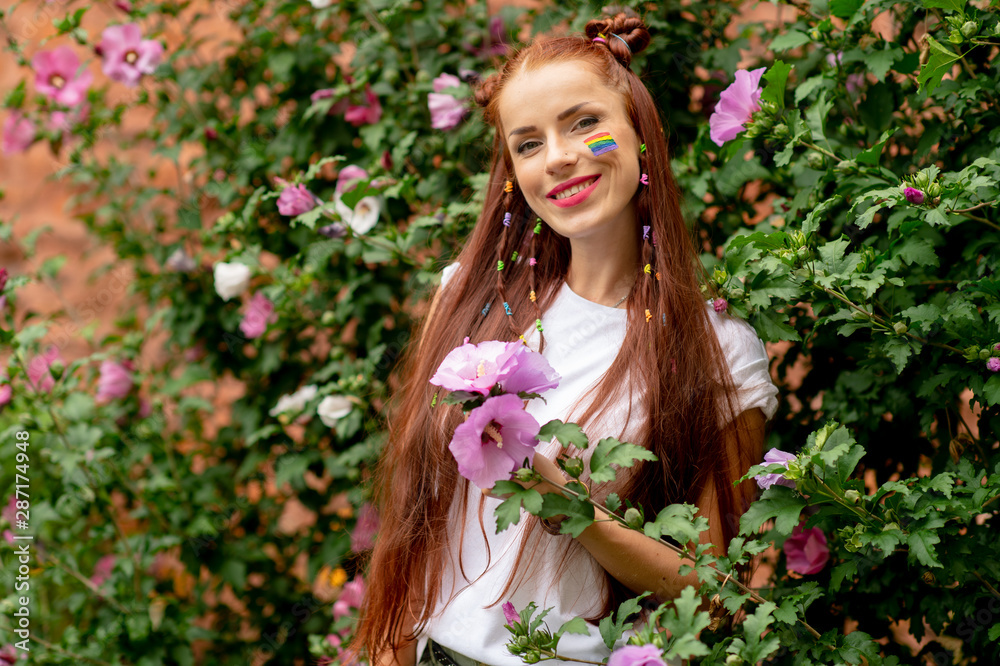 Cheerful lesbian with lgbt rainbow on her face posing in blooming flowers Cheerful lesbian with lgbt rainbow on her face posing in blooming flowers