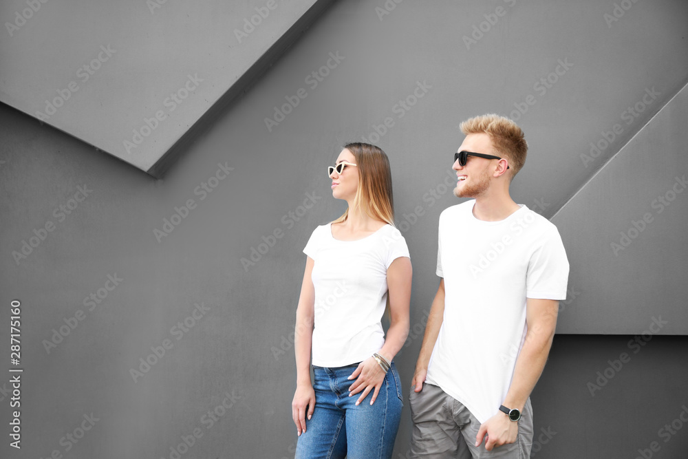 Man and woman in stylish t-shirts near grey wall Man and woman in stylish t-shirts near grey wall