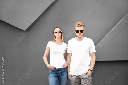 Man and woman in stylish t-shirts near grey wall