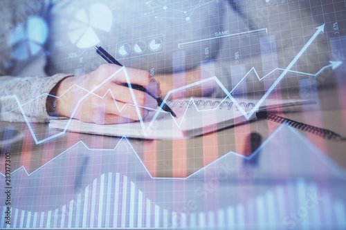 Hands writing information about stock market in notepad. Forex chart holograms in front. Concept of research. Multi exposure