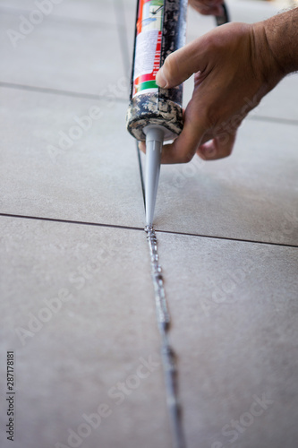 The hand of a construction worker filling the gap between just glued ceramic tiles with silicone