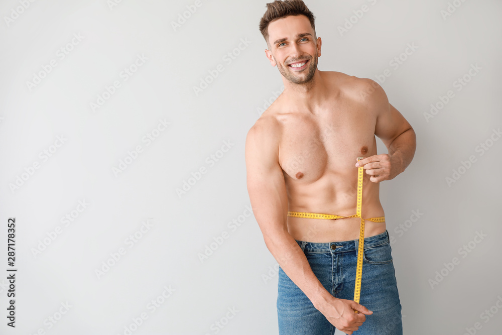 Handsome muscular man with measuring tape on light background. Weight loss concept Handsome muscular man with measuring tape on light background. Weight loss concept