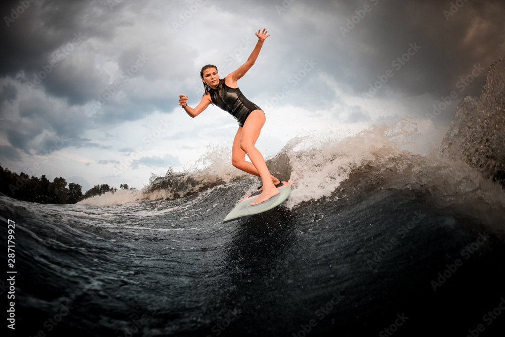 Young girl riding on the wakeboard on the river in the background of trees rising hands