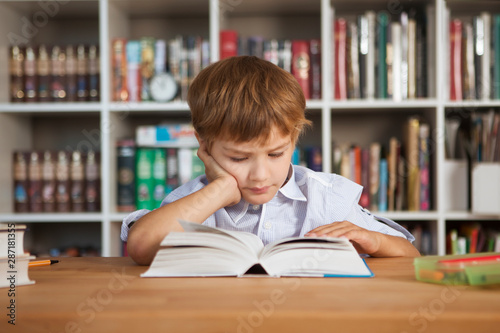 little boy reading book at table in library