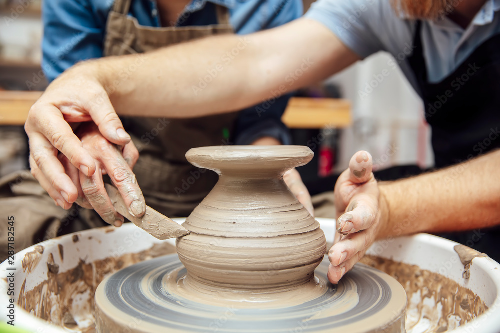 Senior woman spinning clay on a wheel with teacher at pottery class Senior woman spinning clay on a wheel with teacher at pottery class