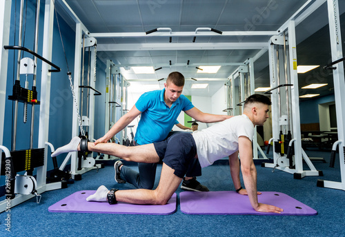 Fototapeta Naklejka Na Ścianę i Meble -  Rehabilitation therapy. Young man doing exercises on mat under supervision of physiotherapist.