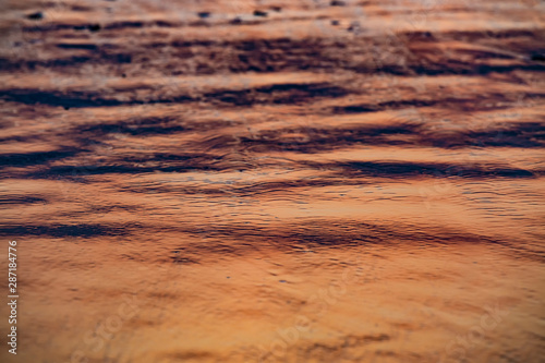 Sea water edge at sunset or sunrise. Texture of waves and sand in the rays of setting sun. Copy space. Selective focus.