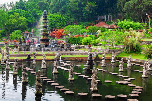 Ancient water palace Tirta Gangga with fountains, natural pools, path in fish pond with statues of dancing women in traditional costumes. Culture, arts of Bali, popular travel destination in Indonesia photo