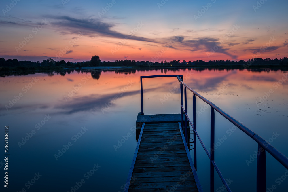 Jetty with a handrail on the lake, horizon and evening colorful clouds on the sky Jetty with a handrail on the lake, horizon and evening colorful clouds on the sky