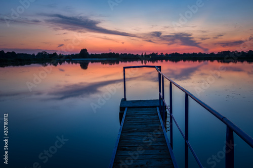 Jetty with a handrail on the lake, horizon and evening colorful clouds on the sky