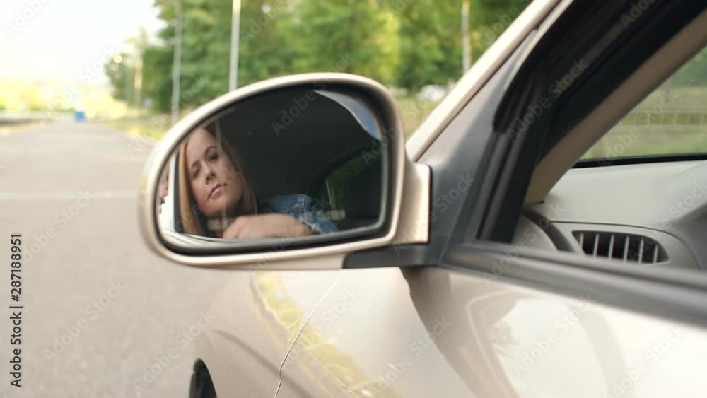 Reflection of a young woman in a side mirror of a car, she straightens her hair. Beautiful woman looking in car back rear-view mirror sitting in vehicle. Slow motion. Reflection of a young woman in a side mirror of a car, she straightens her hair. Beautiful woman looking in car back rear-view mirror sitting in vehicle. Slow motion.