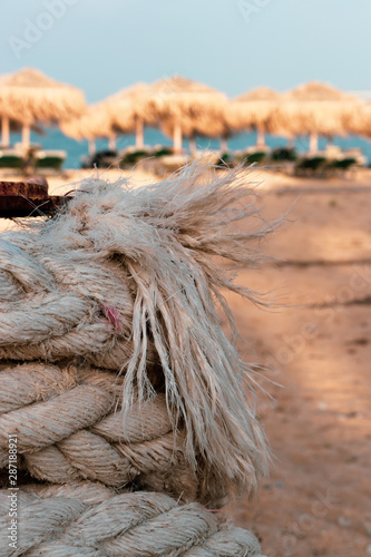 closeup of an old rope rolled up on a metal rod kind of mooring equipment sandy beach and the sea int the background with beach beds and umbrellas photo