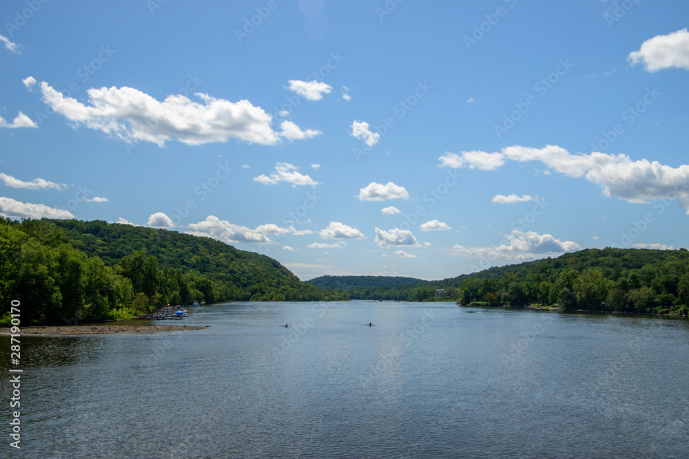 Wide angle view of the Delaware River near New Hope, Pennsylvania showing a wide body of deep blue water with tree covered hills in the background. There are boaters seen on the river