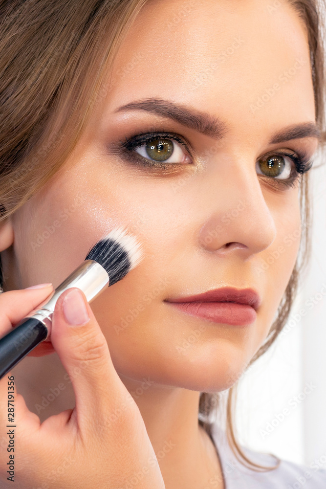 Professional makeup artist working with client in salon. Makeup artist applies highlighter on the face of a girl Professional makeup artist working with client in salon. Makeup artist applies highlighter on the face of a girl