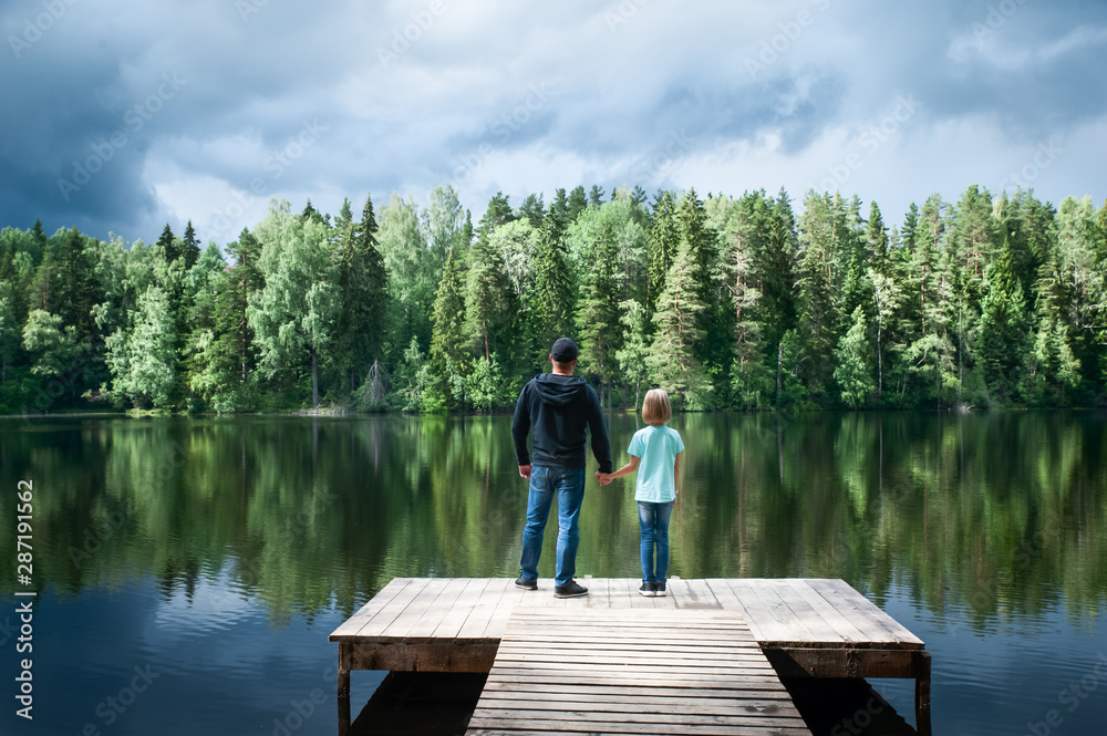 Father with a small daughter are standing on the pier of a beautiful lake, the father is opening a new world for his daughter. Father and daughter relationship concept Father with a small daughter are standing on the pier of a beautiful lake, the father is opening a new world for his daughter. Father and daughter relationship concept