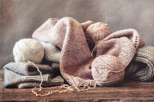 Woolen threads in balls and knitted sweaters on a wooden background, the concept of hobby and needlework handmade