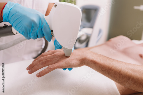Konstfotografi Cropped shot of a cosmetologist removing hair on the hand of a male client, usin