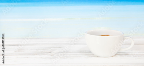 Coffee cup on white wood table with bright blue sea background