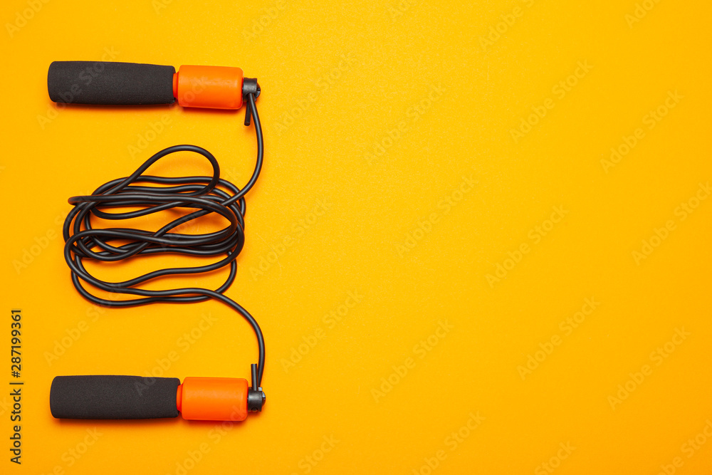 Jump rope. Fun exercises for body health. Orange rope with black cord. Yellow orange background Jump rope. Fun exercises for body health. Orange rope with black cord. Yellow orange background