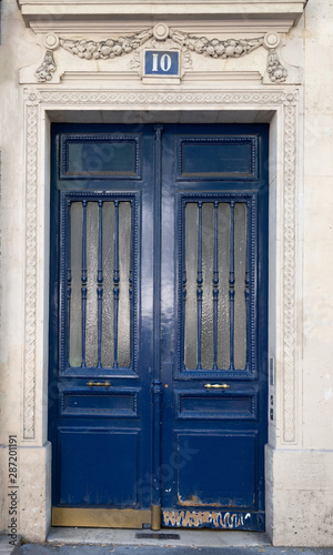Old blue door. Doorway with door windows with matte glass protected by vertical patterned grids. Dark blue painted antique door with shabby bottom part. Antique building in Paris France.  © Ninel