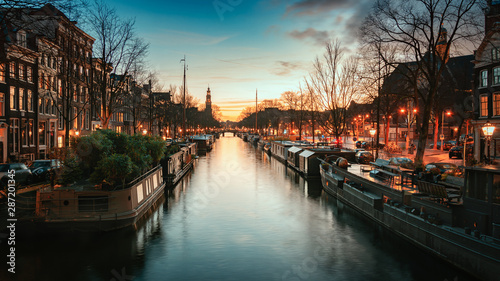 Houseboats in the Prinsengracht in the old center of Amsterdam with the spire of the Westertoren in the background during sunset