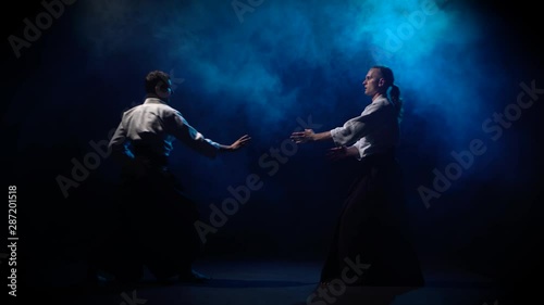 Two fighters participants of the training in special clothes of aikido hakama work out the methods of single combat on blue smoke background. photo