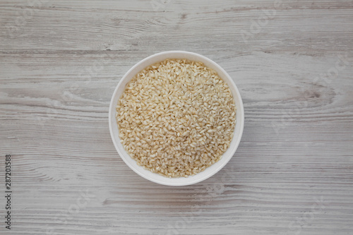 Organic Arborio rice in a white bowl on a white wooden background, top view. Flat lay, overhead, from above.