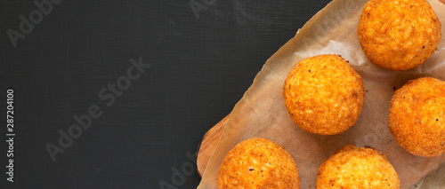 Homemade fried Arancini on a rustic wooden board on a black background, top view. Italian rice balls. Flat lay, from above, overhead. Space for text.