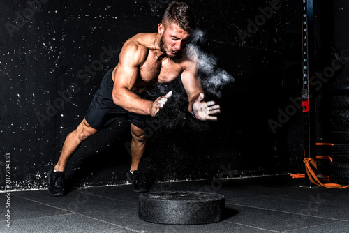 Young muscular man with big sweaty muscles doing push ups workout training with clap his hand above the barbell weight plate on the gym floor with motion blur