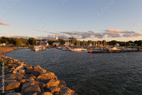  Pretty Saint-Michel-de-Bellechasse marina seen during a late afternoon summer golden hour, with sailboats, historical 1873 church and other buildings in the background, Quebec, Canada
